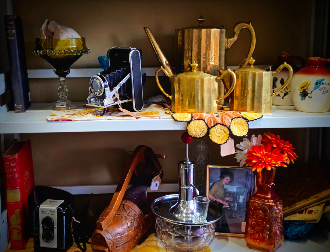 Vintage antique shop shelf with brass tea set, old cameras, books, flowers, and nostalgic keepsakes for last-minute Mother’s Day gift inspiration.