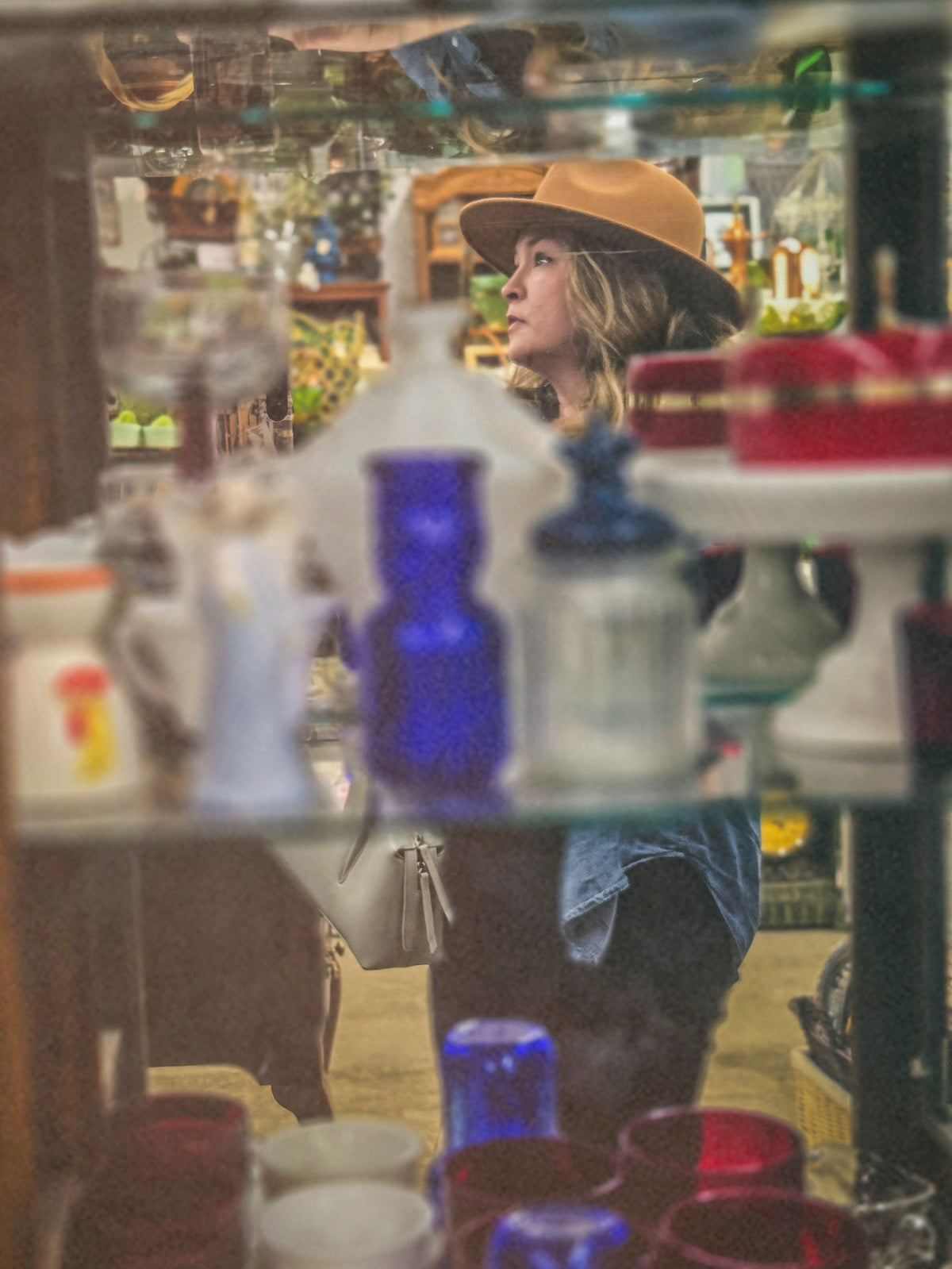 Vintage Hearts Club founder reflected in a mirror among vintage glassware in an antique shop